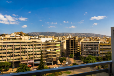 Vue panoramique sur le centre-ville d'Athènes avec ses immeubles modernes et les collines environnantes en arrière-plan.